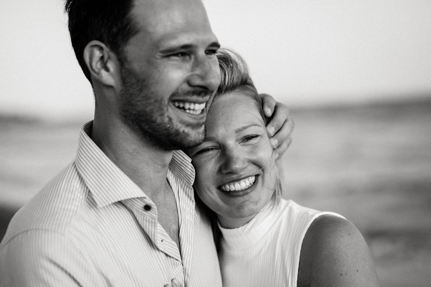 A romantic black and white portrait of a couple laughing together on the beach.