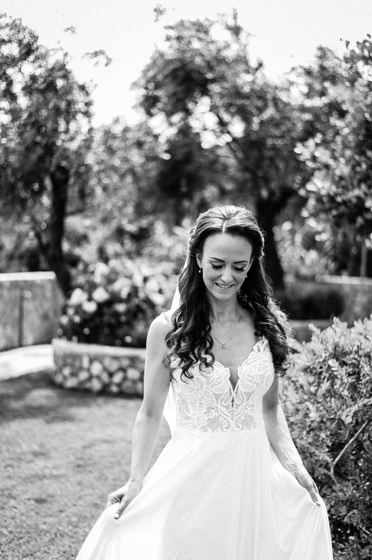 A black and white photograph of a flowing white wedding dress in a garden setting.