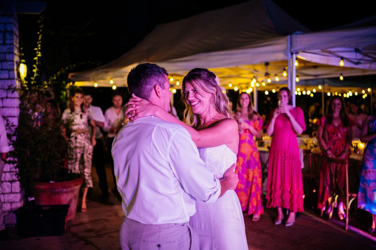 Romantic first dance moment under warm tent lighting at evening wedding reception.