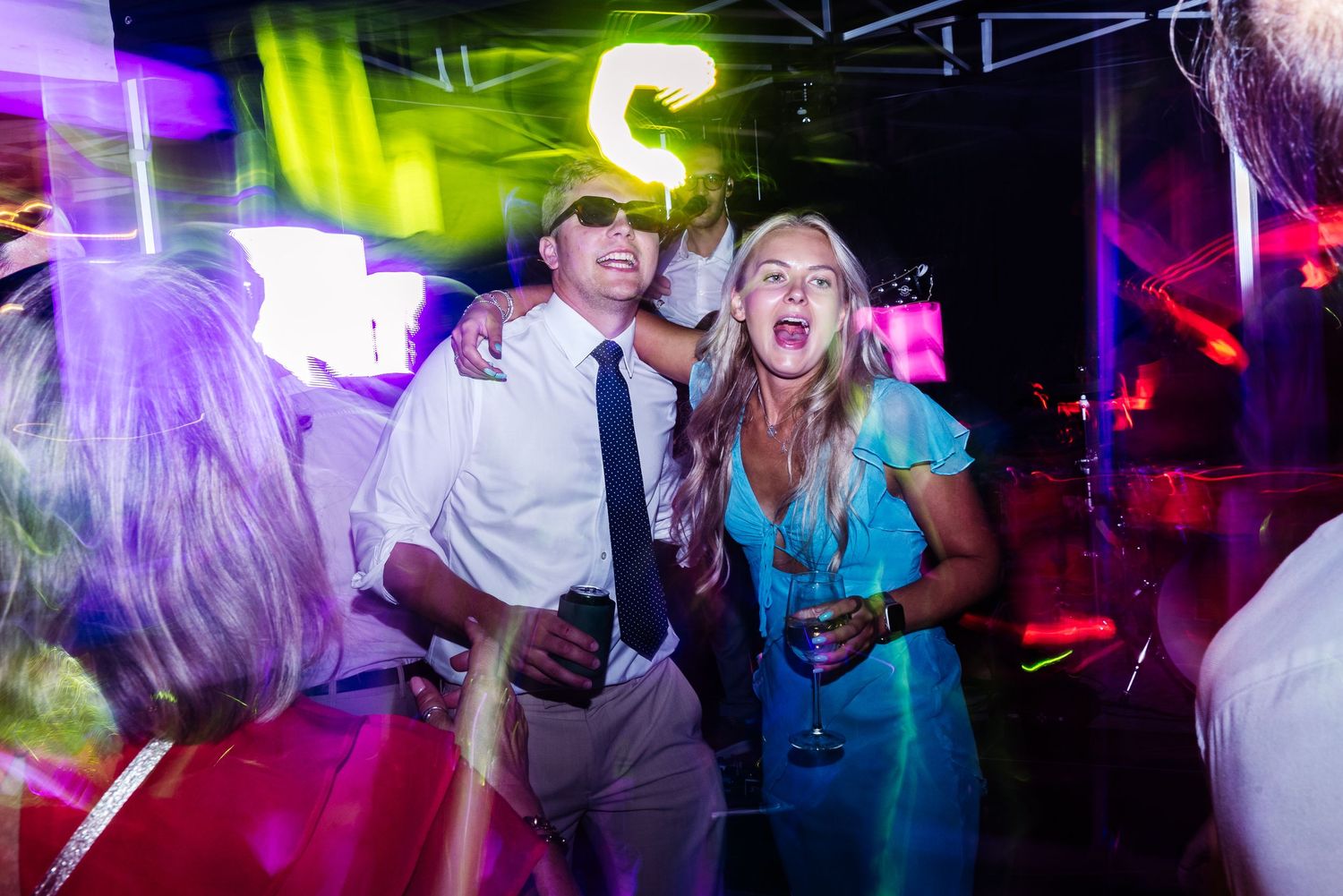 Wedding guests dancing and celebrating under vibrant neon lights at night reception.