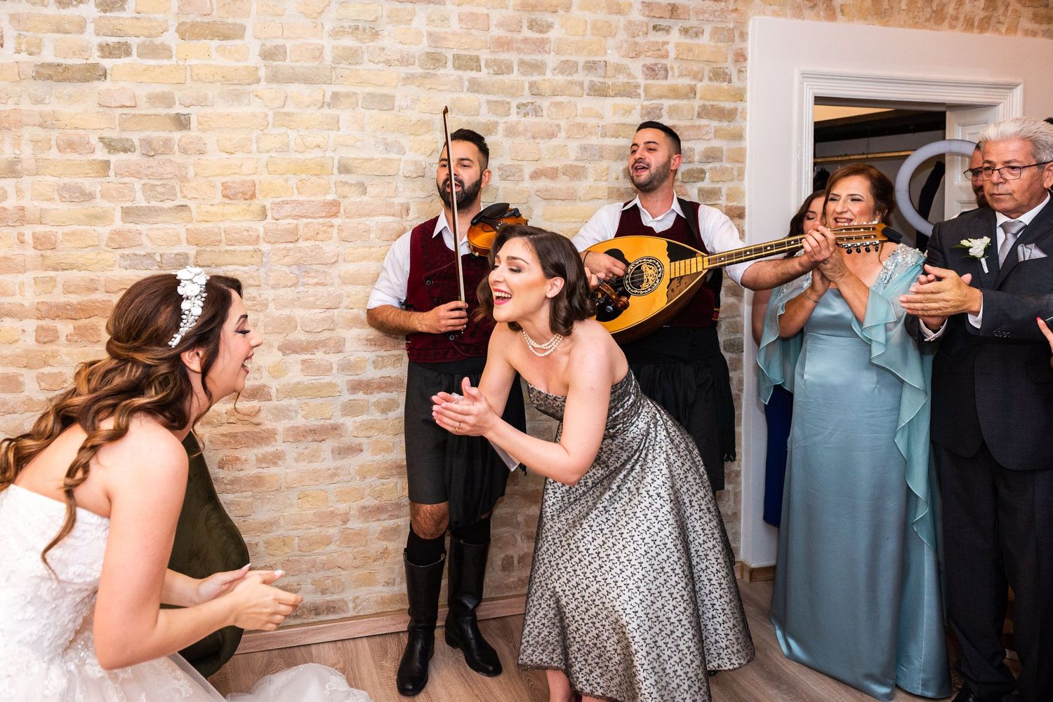 Wedding guests gather and pose with fans in front of an exposed brick wall.