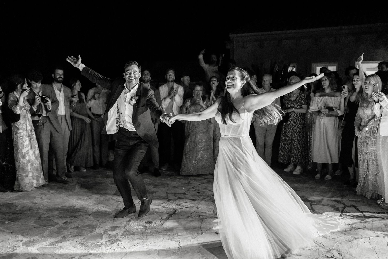 Wedding party dancing and celebrating on a rustic outdoor dance floor at night.