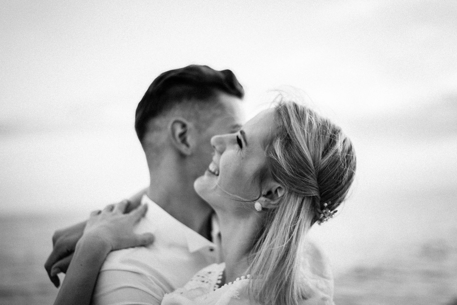 Romantic black and white portrait of a couple embracing against a cloudy sky.