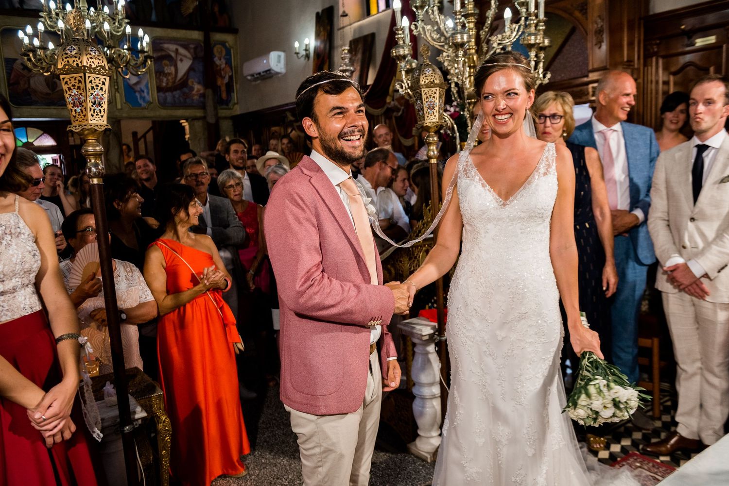 Wedding ceremony in an ornate venue with guests in colorful attire watching the celebration.