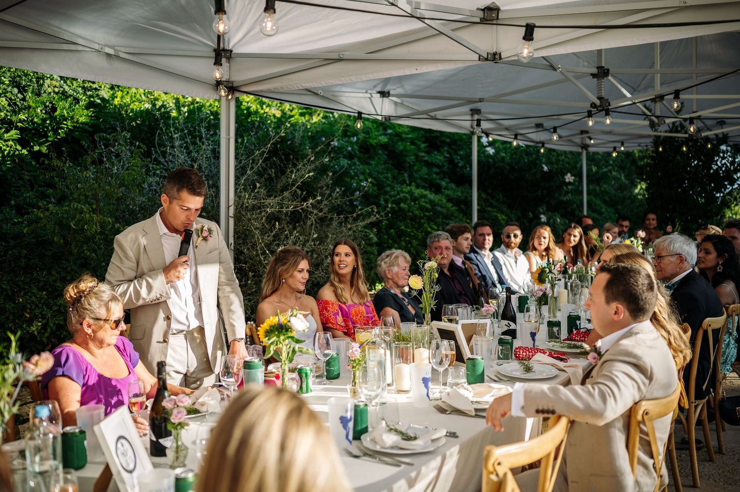 Guests seated at long tables under white tents during an outdoor wedding reception.