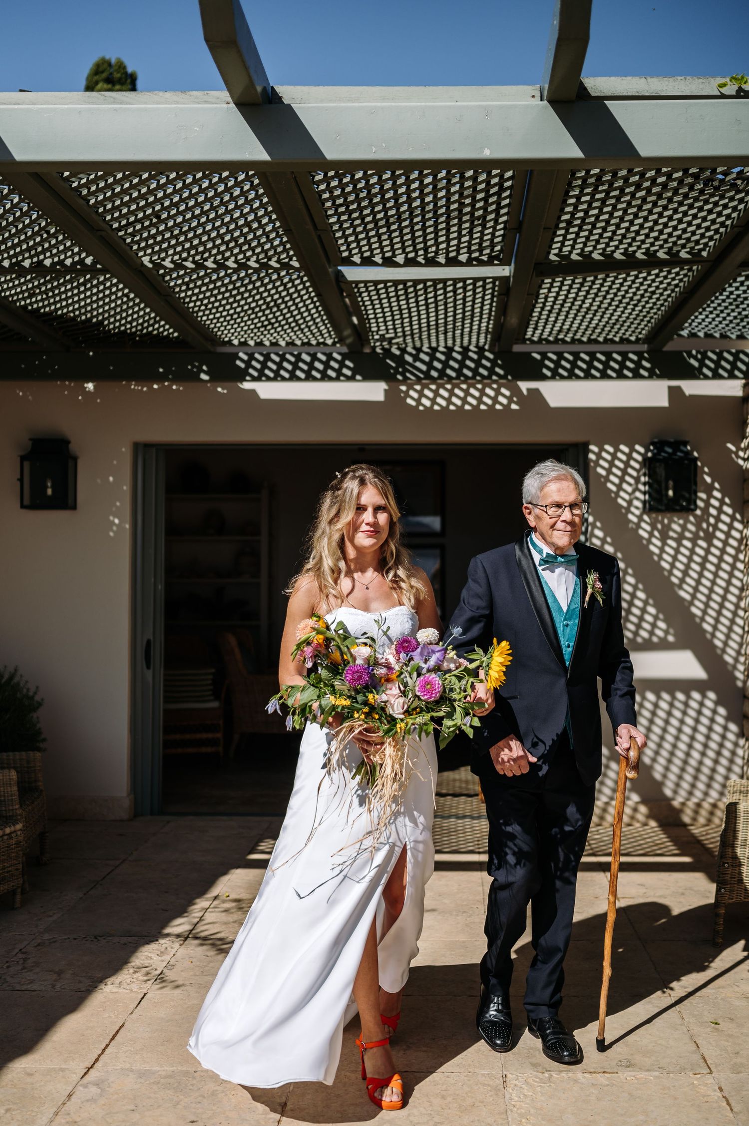Outdoor wedding ceremony under pergola with dramatic shadow patterns.