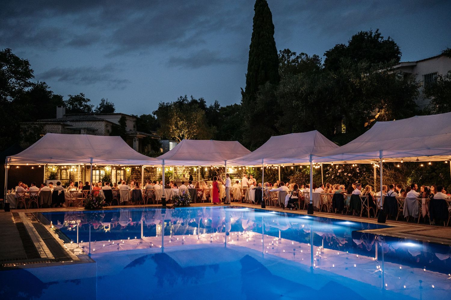 Wedding celebration at night with white tents and glowing pool creating romantic ambiance.