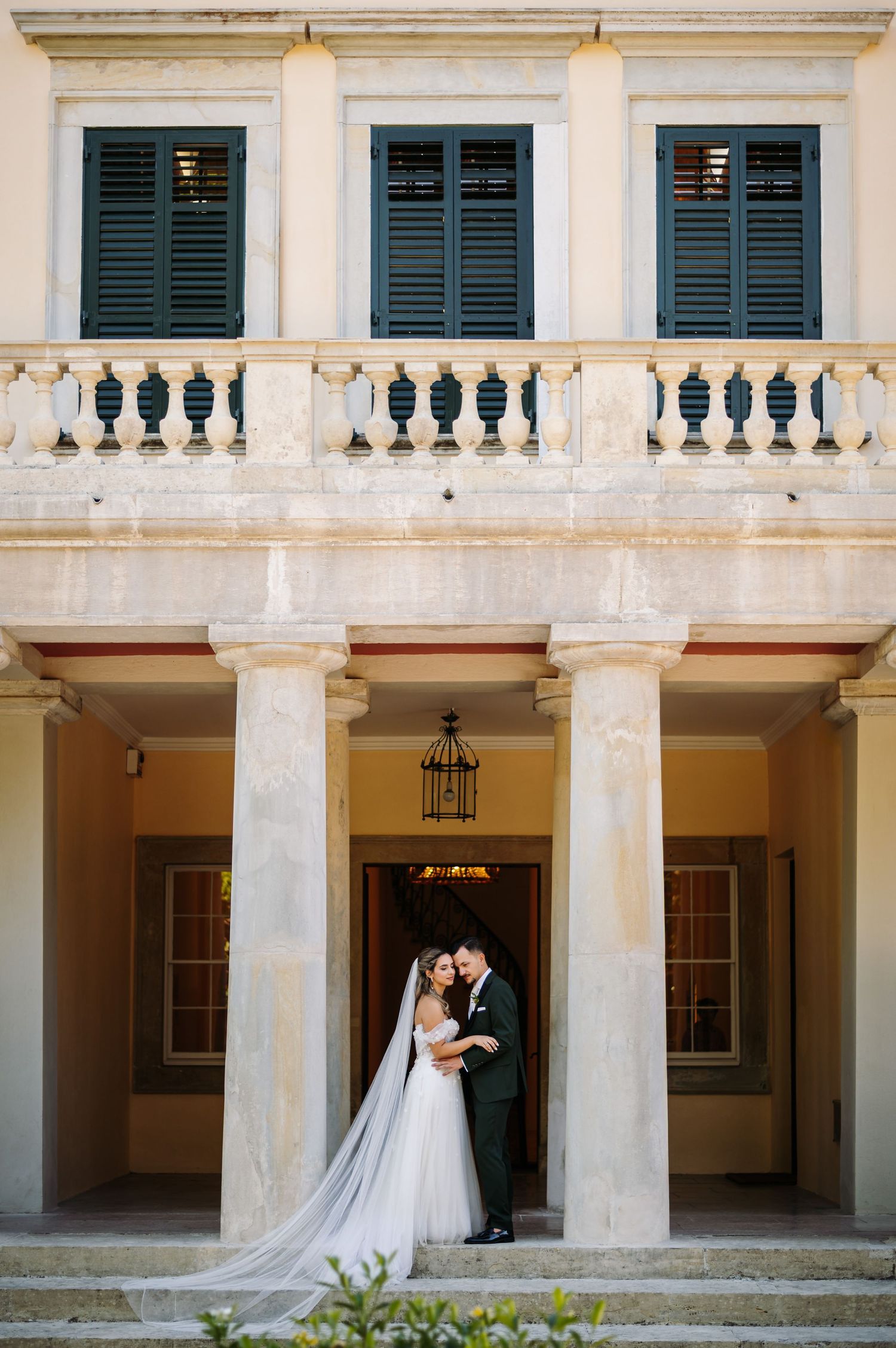 Elegant wedding couple poses in a classic colonnade with white pillars and dramatic lighting.
