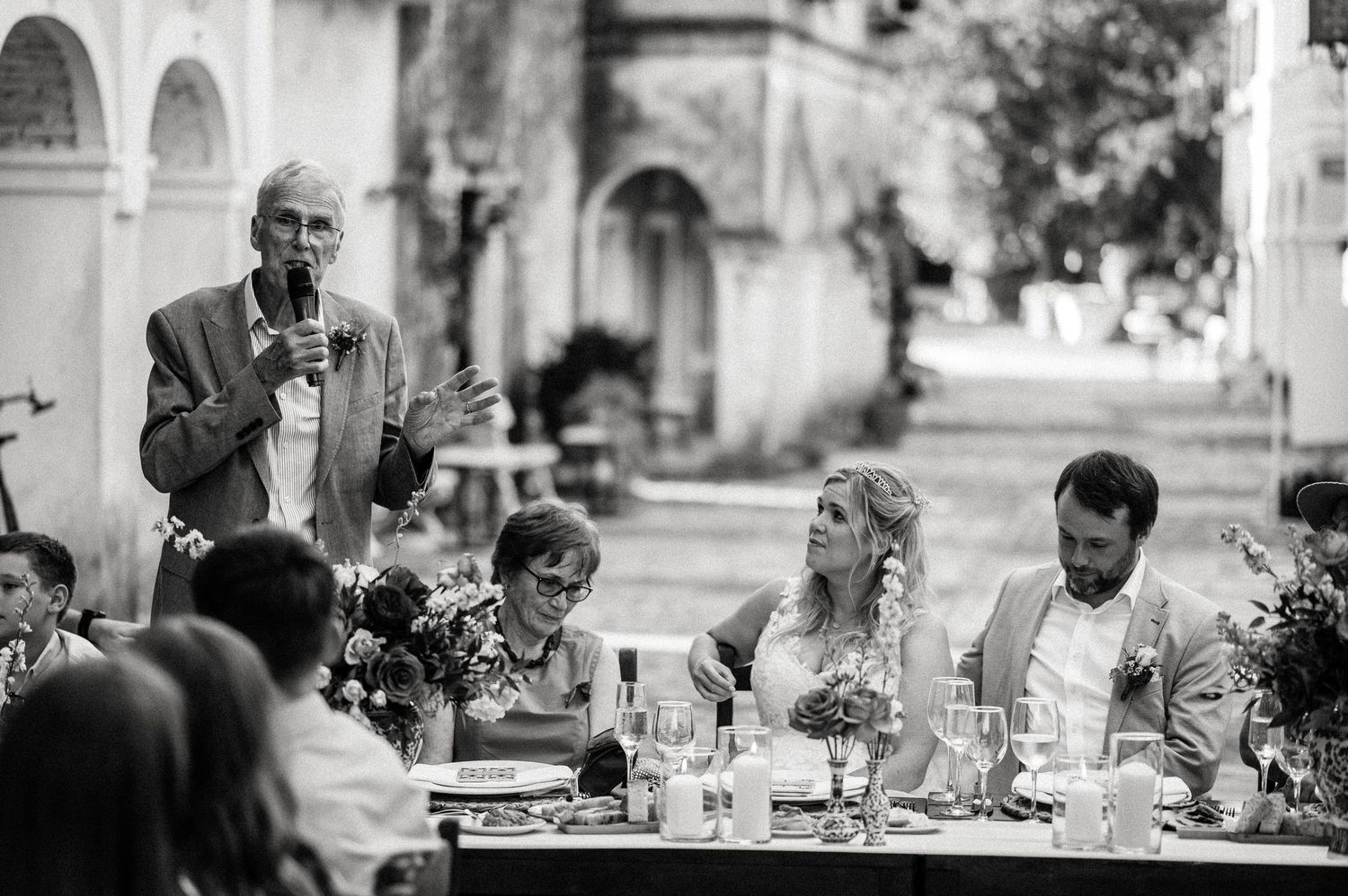 Black and white candid photo of guests enjoying an outdoor wedding reception dinner.