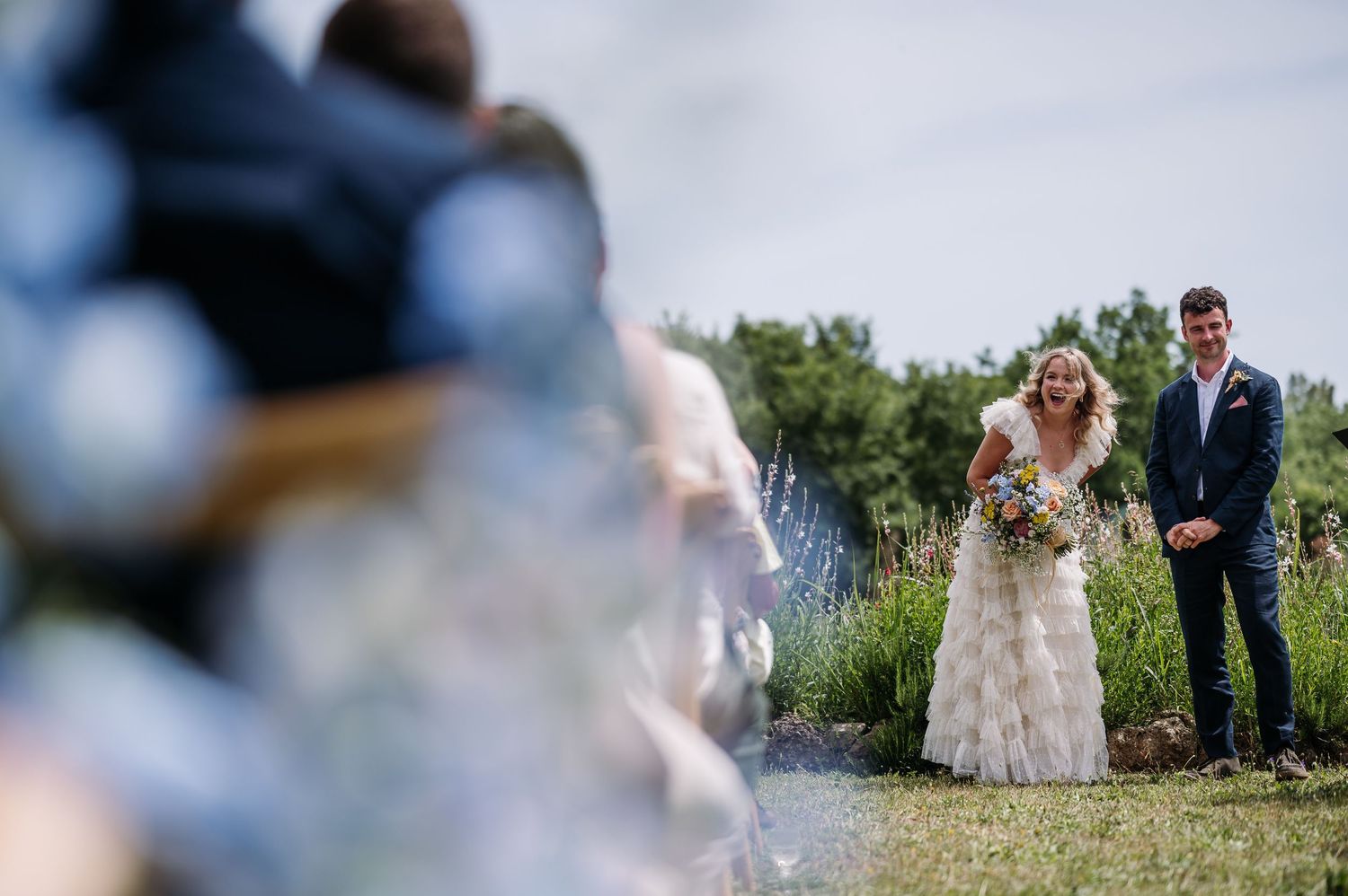 Scenic outdoor wedding ceremony setup with guests seated in wooden chairs against a natural backdrop.