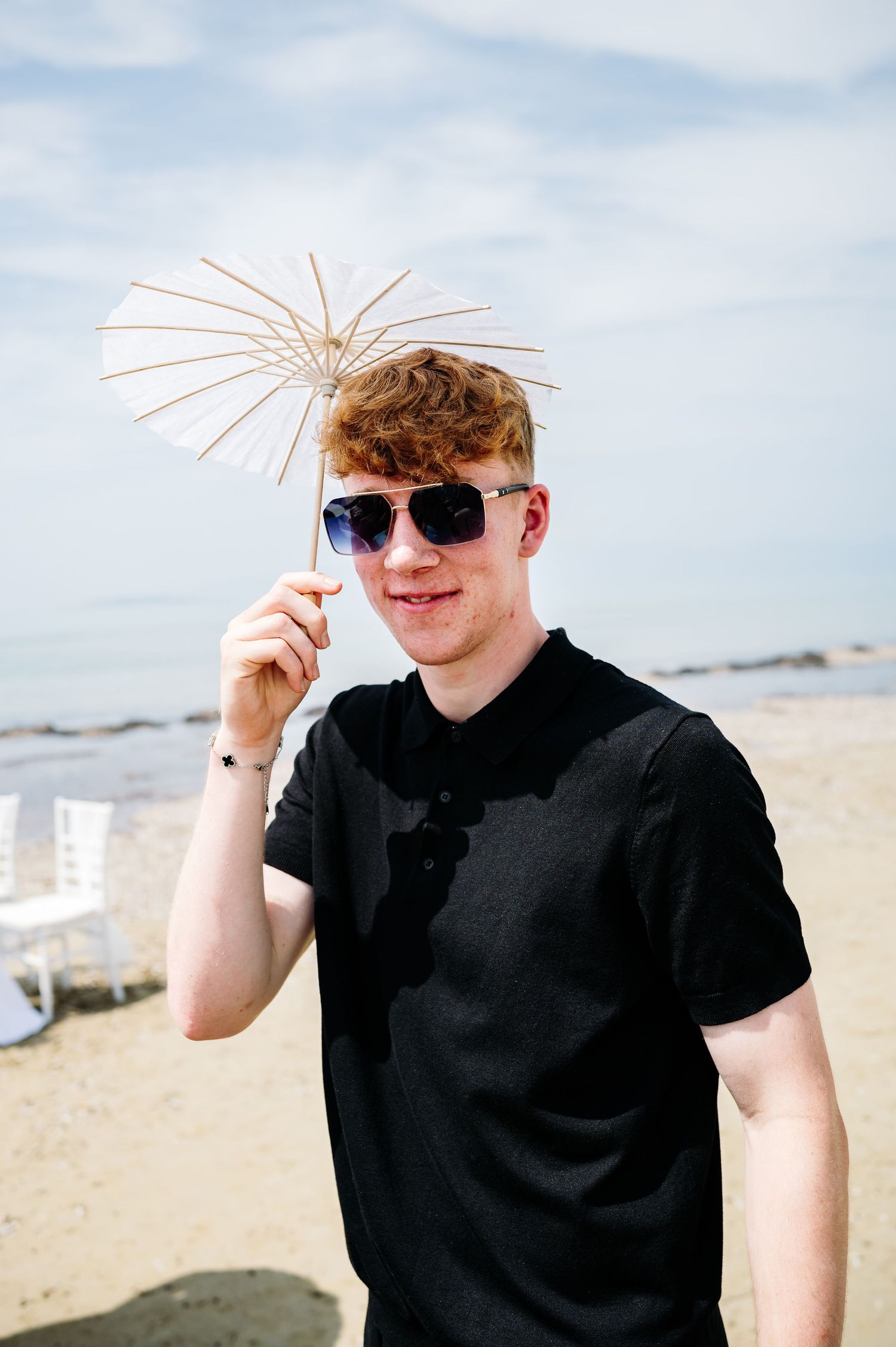 Person in black shirt poses with decorative parasol on sunny beach.