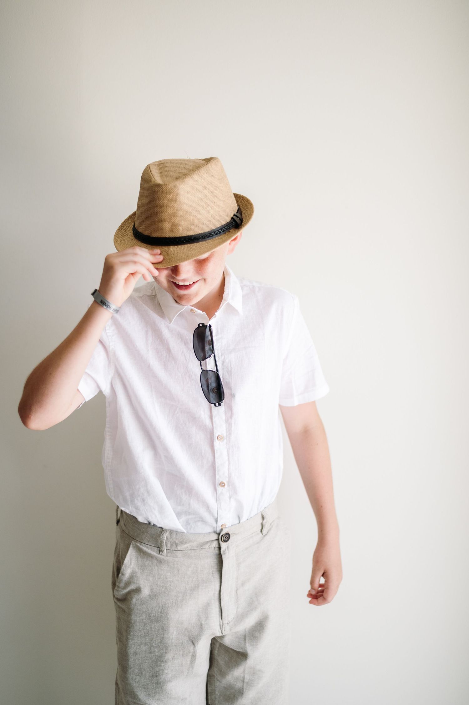 Stylish wedding attire featuring a white shirt, straw hat, and light colored pants against a white background.