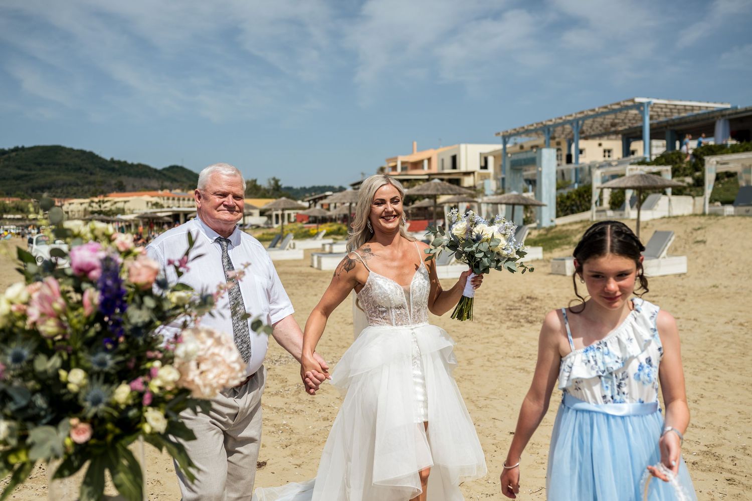 Beach wedding ceremony setup with guests and floral decorations by the ocean.