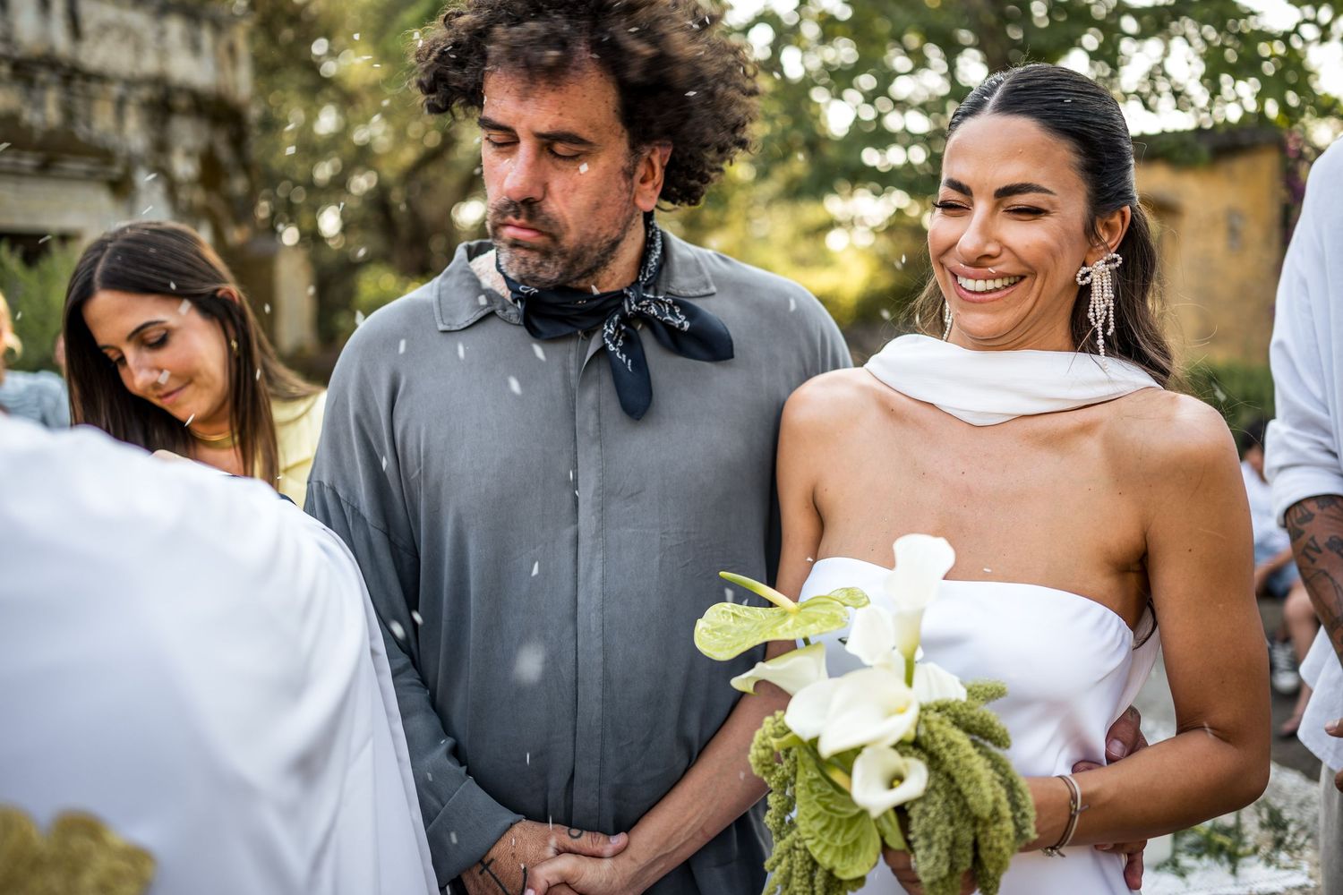 Wedding party members share intimate moments during an outdoor garden ceremony.