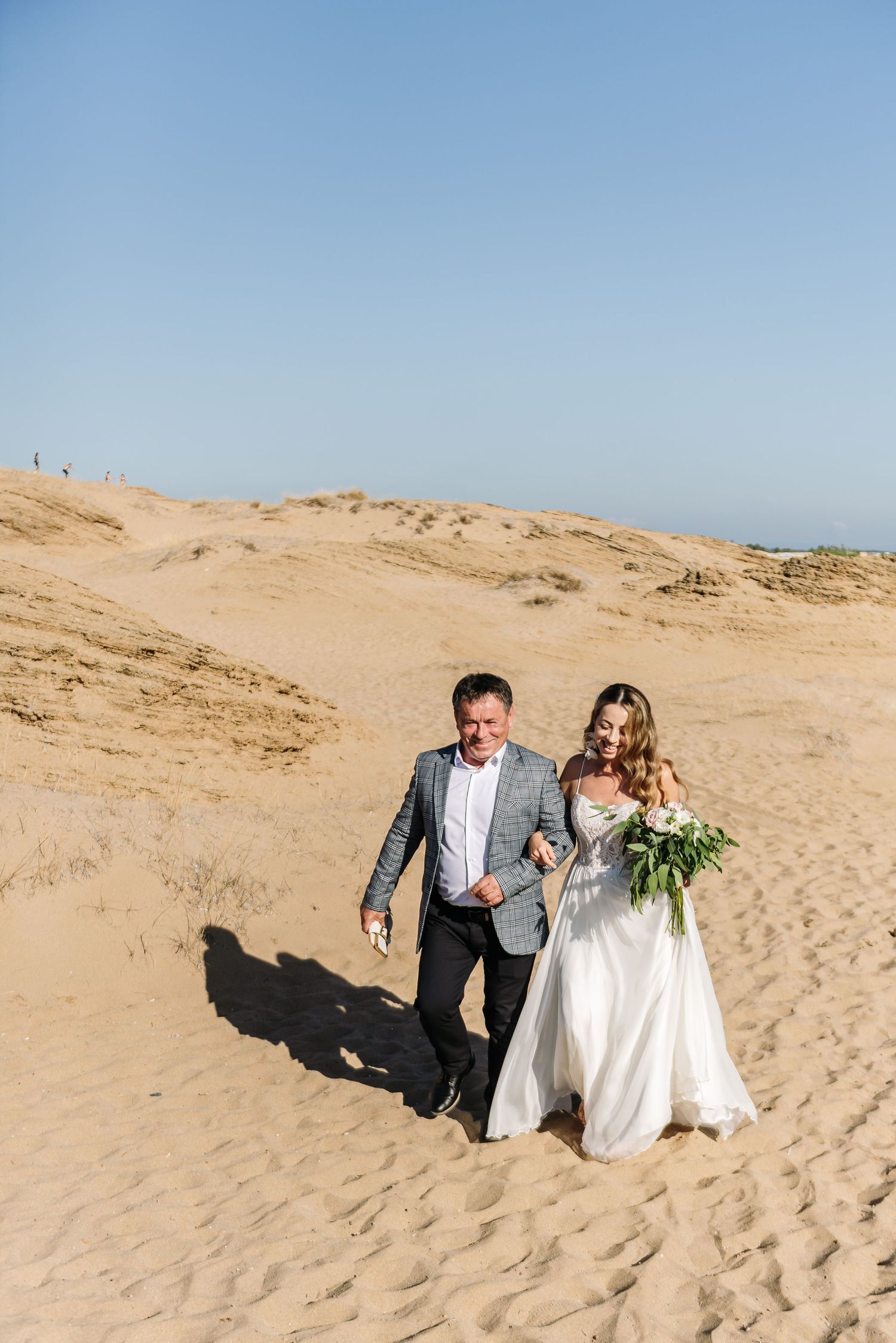 Wedding party walking through scenic sand dunes under bright blue sky.