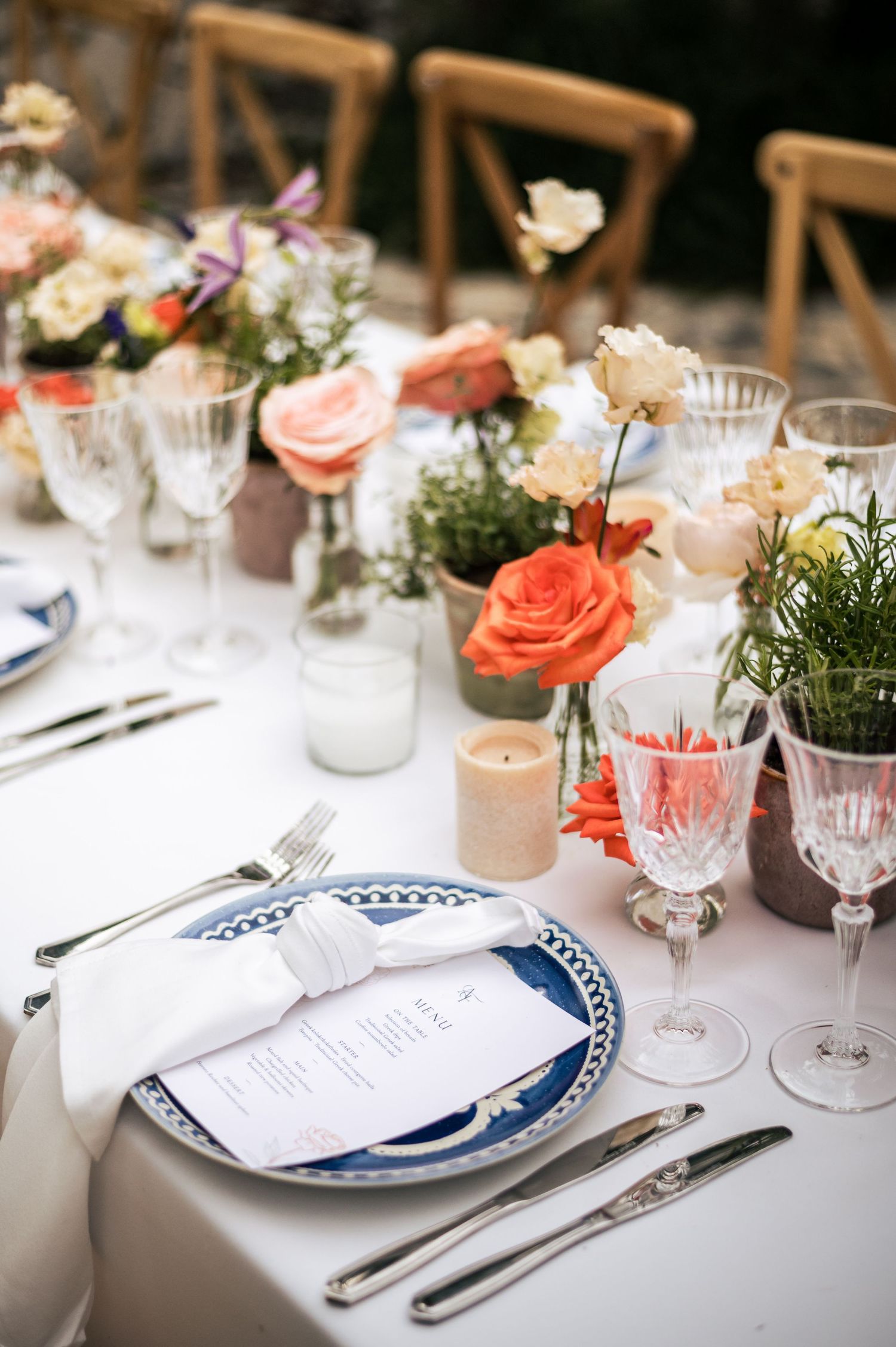 Elegant place settings with blue and white plates, crystal glasses, and coral floral accents.
