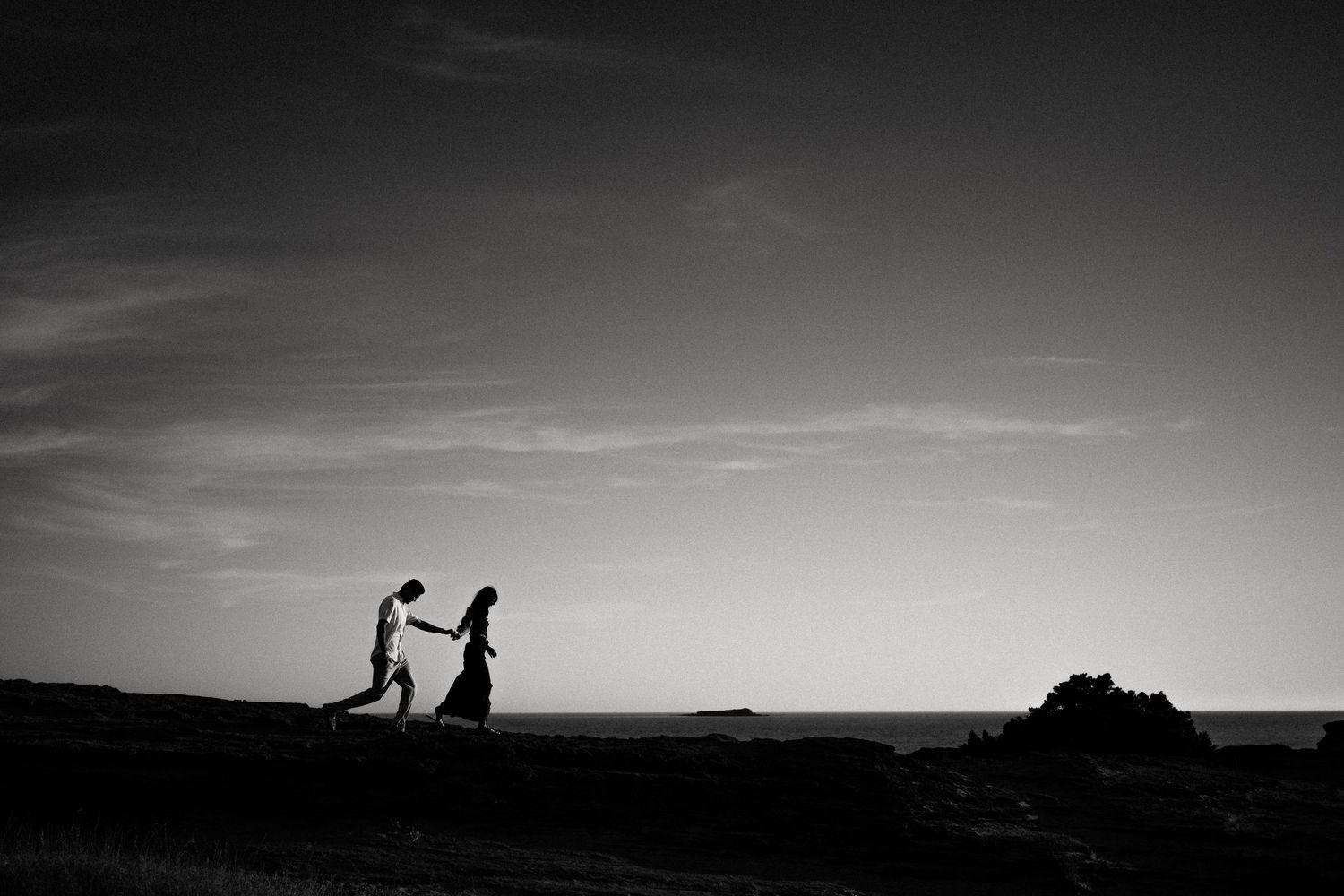 Silhouetted couple walking along a scenic mountain ridge at sunset.