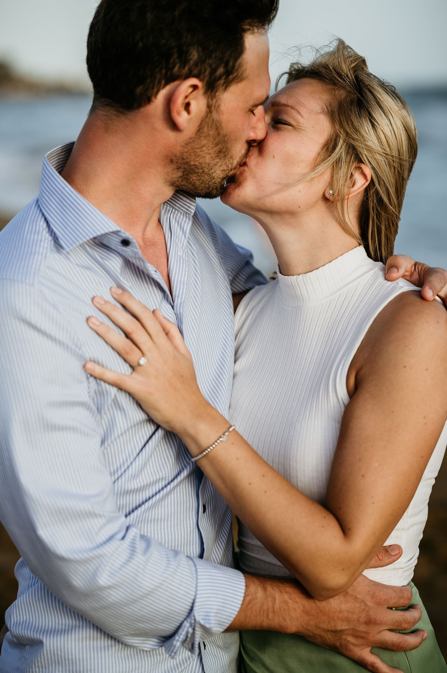 Romantic kiss shared between a couple against an ocean backdrop.