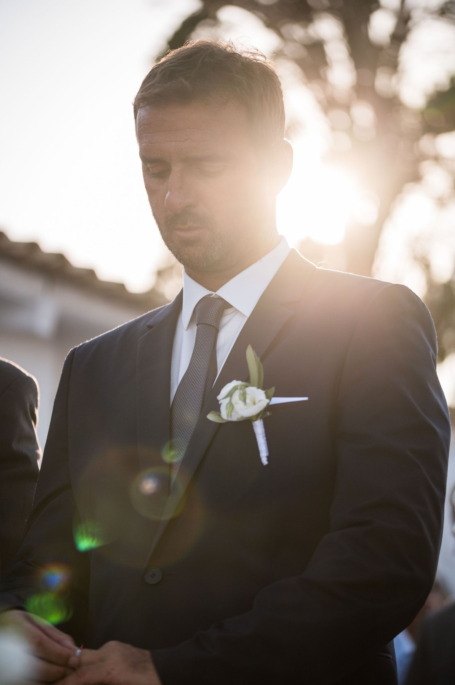 Elegant wedding party members in black suits standing in golden sunlight during sunset ceremony.
