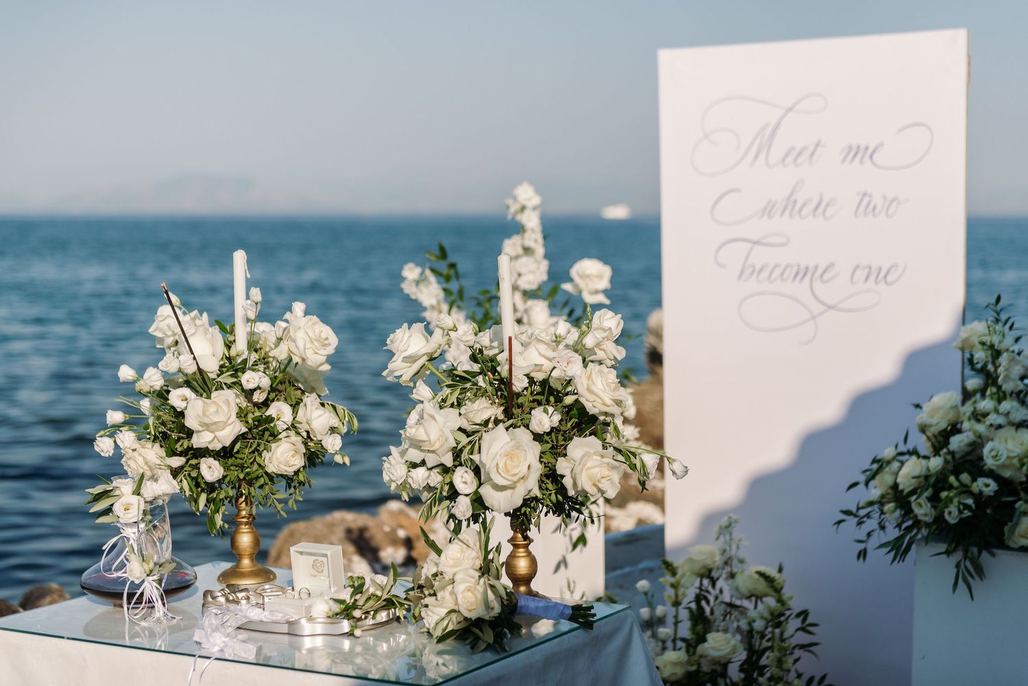 Elegant white floral centerpieces and wedding decor arrangements displayed against an ocean view.