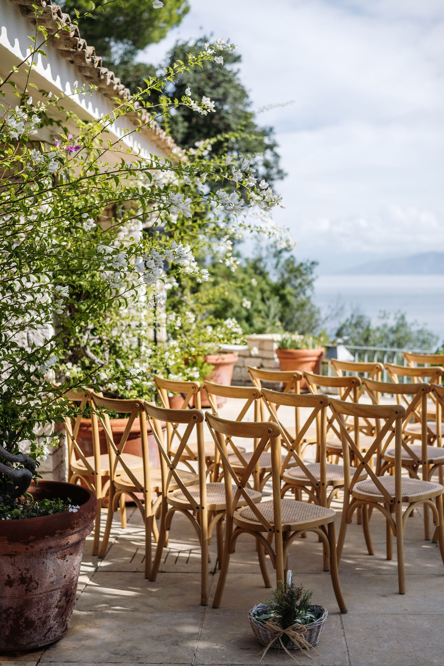 Rustic wooden chairs set up on a stone terrace overlooking a scenic coastal landscape.