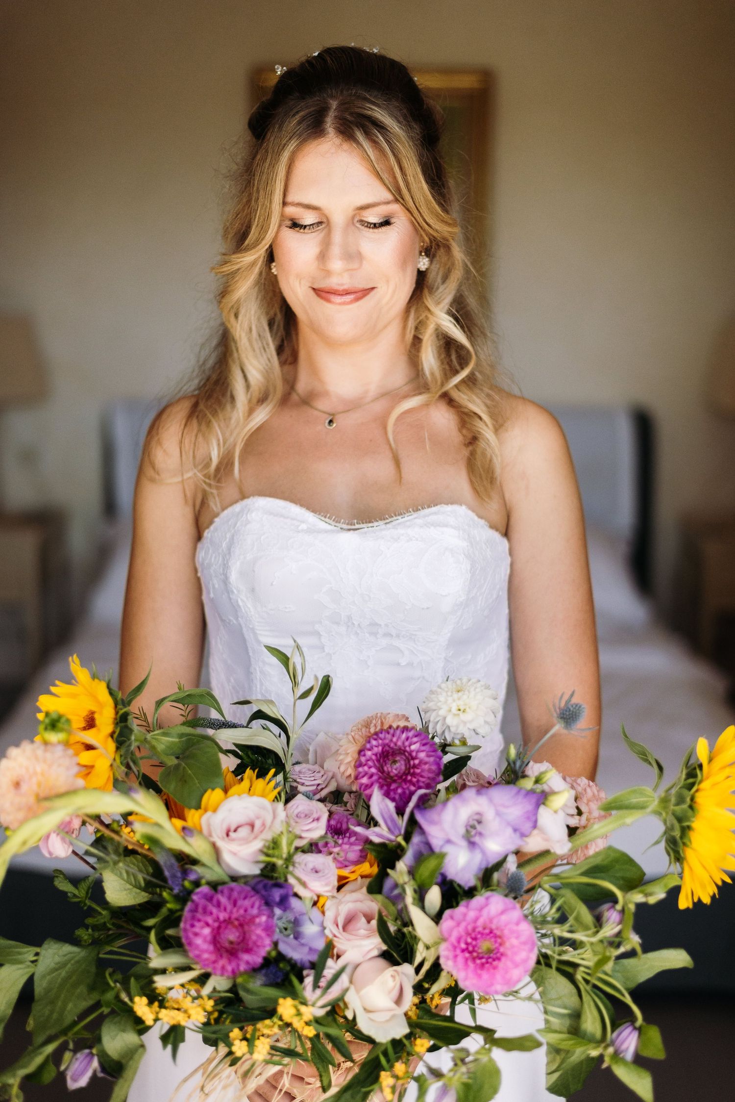 Beautiful wedding bouquet with vibrant sunflowers, pink dahlias and mixed flowers against white dress.