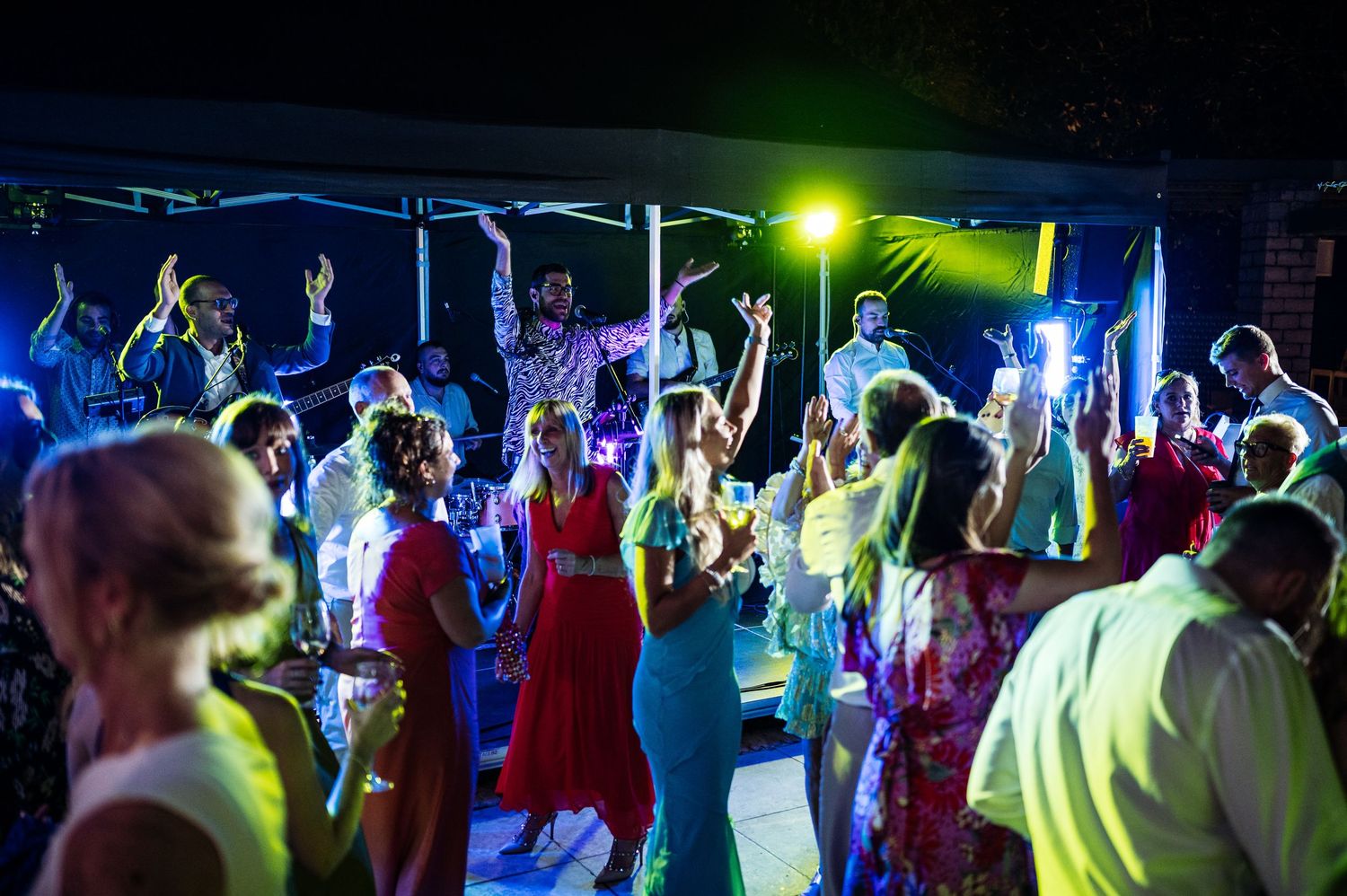 Energetic dance party with colorful lighting and crowd of guests dancing under tent.