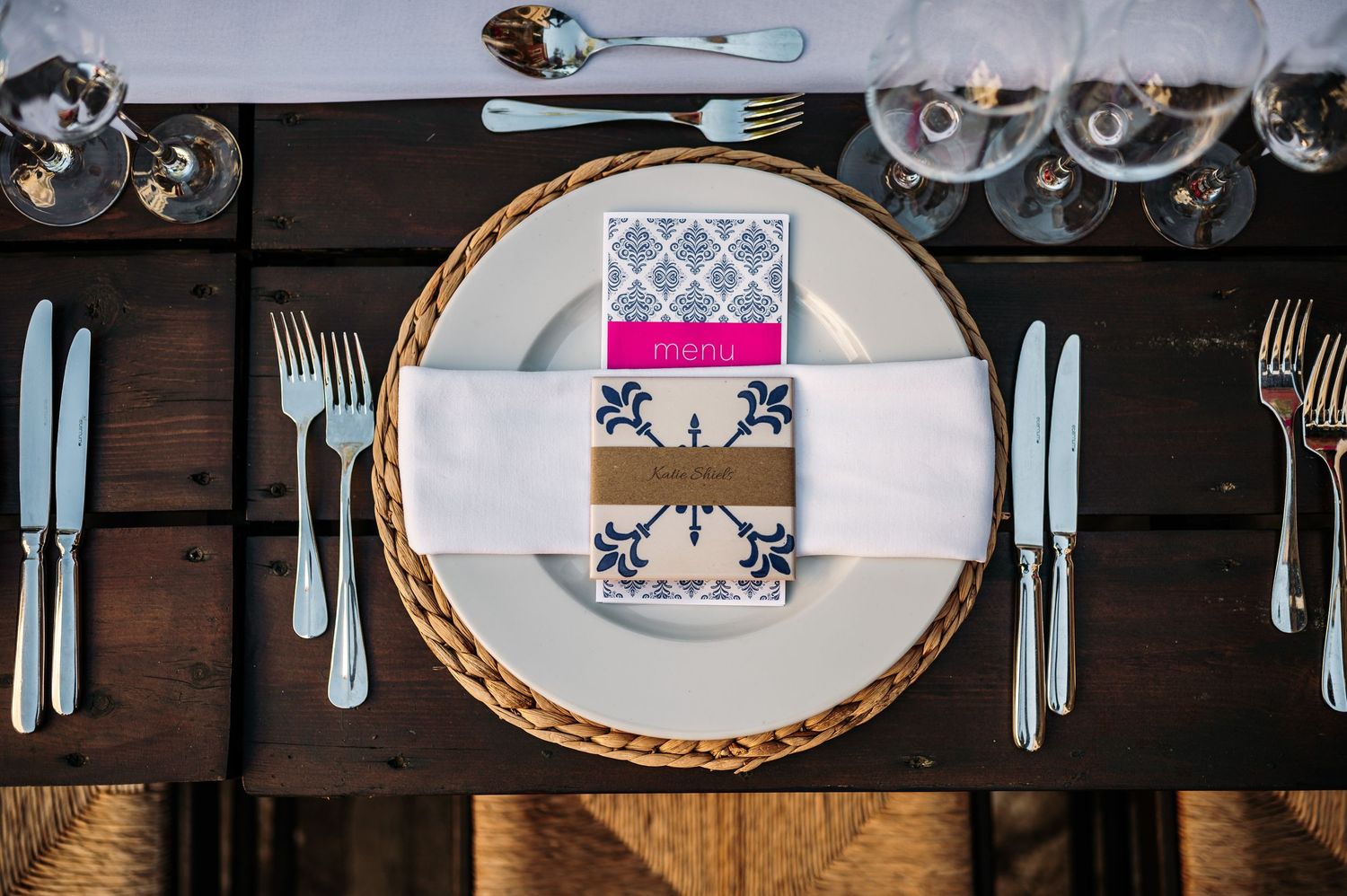 Elegant place setting with patterned plates, blue cutlery and decorative napkin on wooden table.