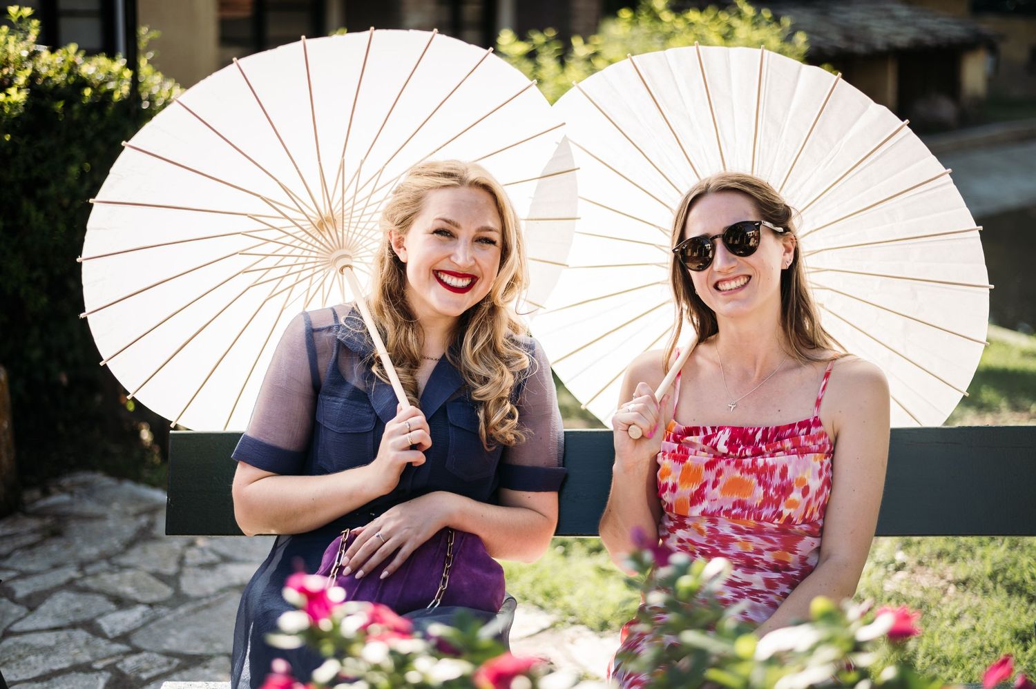 Ladies with white parasols enjoying a sunny garden party in floral dresses.