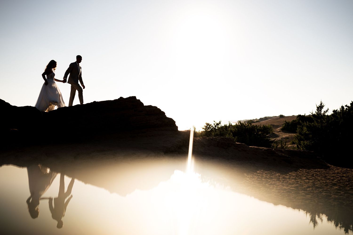 Romantic silhouettes against bright sky in seaside wedding portraits.