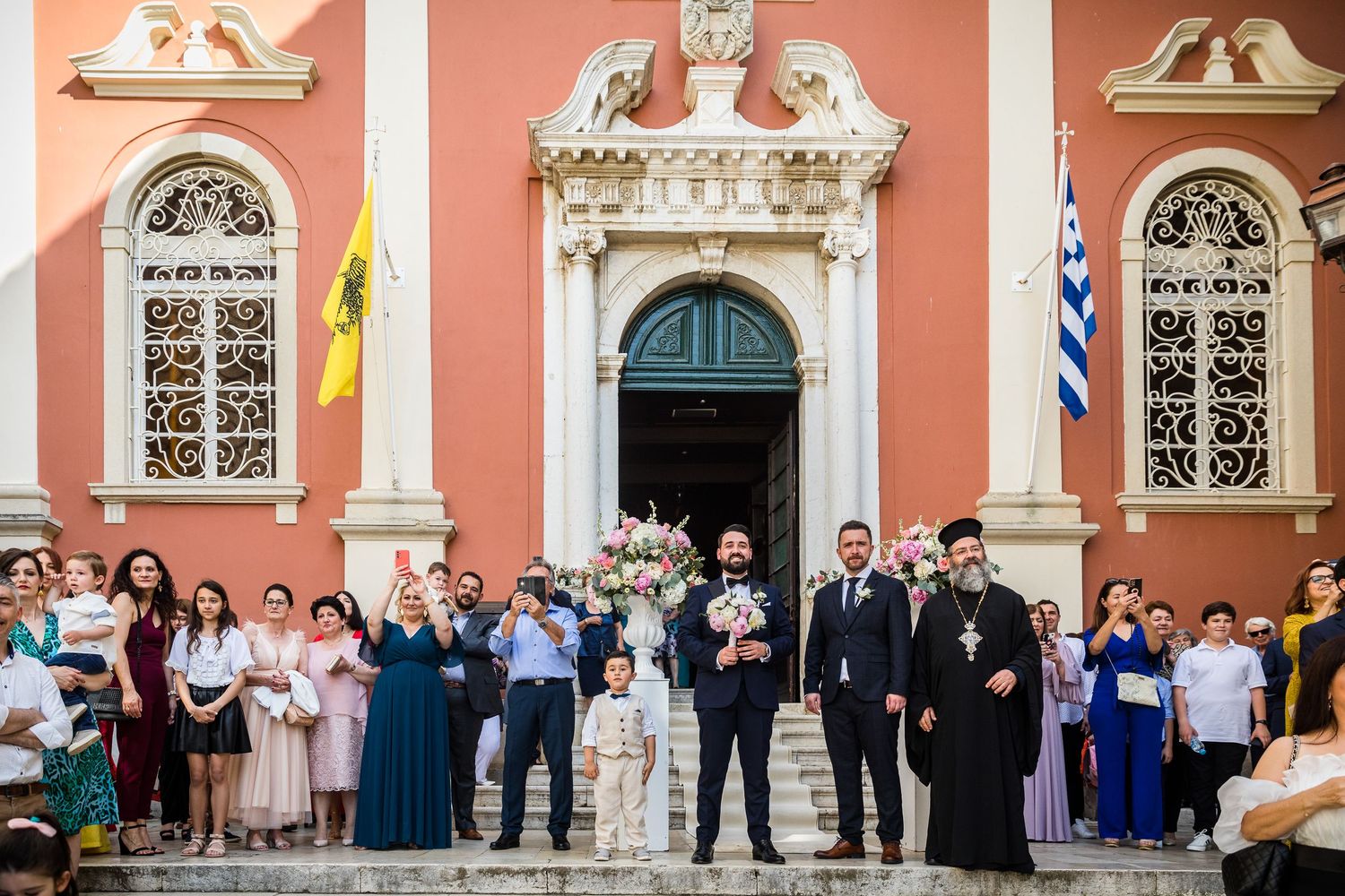 Wedding party lined up against a pink building facade with ornate architectural details.