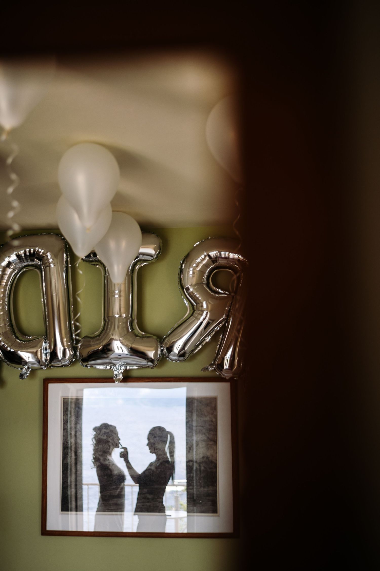Silver balloon letters and white balloons decorating a wall with framed photos.