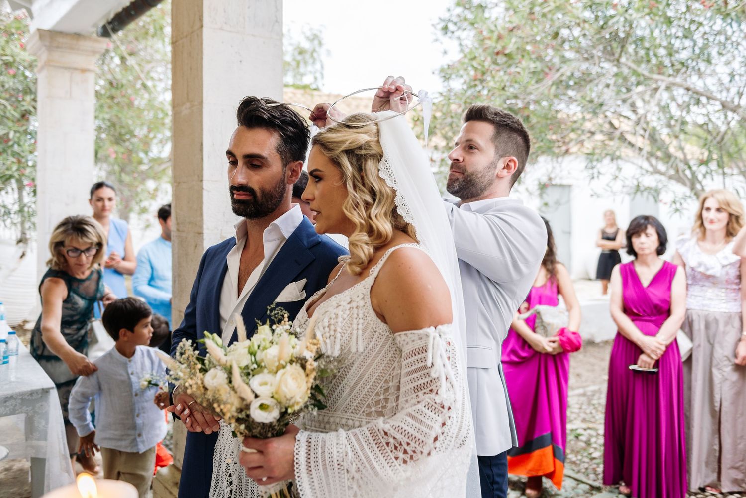 Wedding reception celebration under white Mediterranean archways with colorful guest attire.