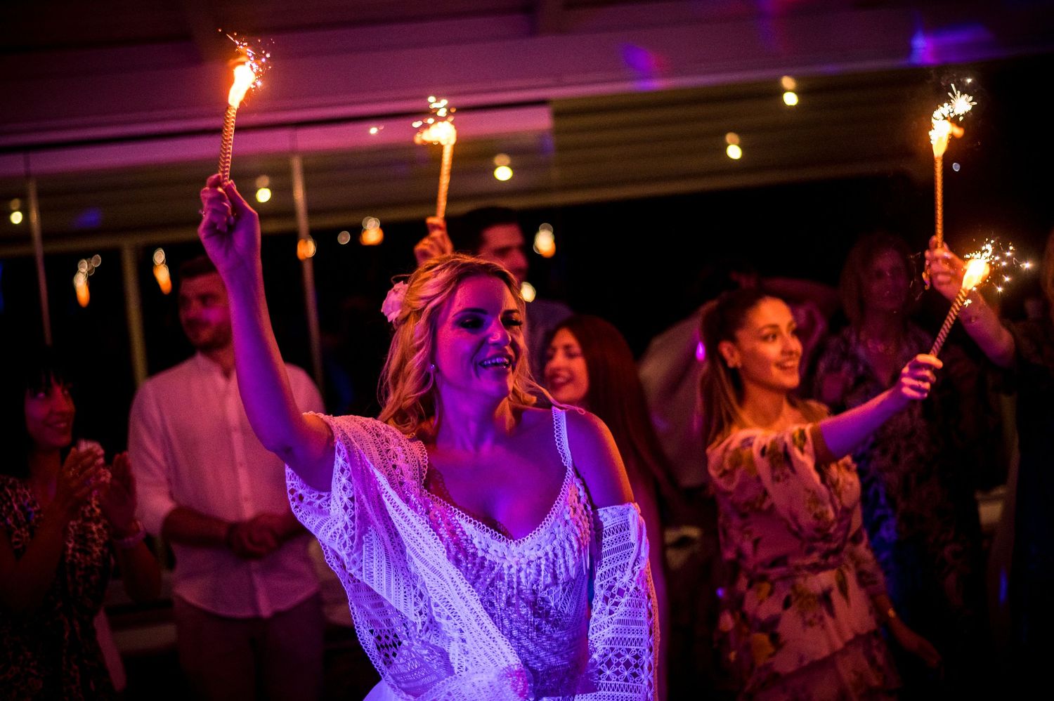 Wedding celebration with sparklers creating a magical atmosphere under purple lighting.