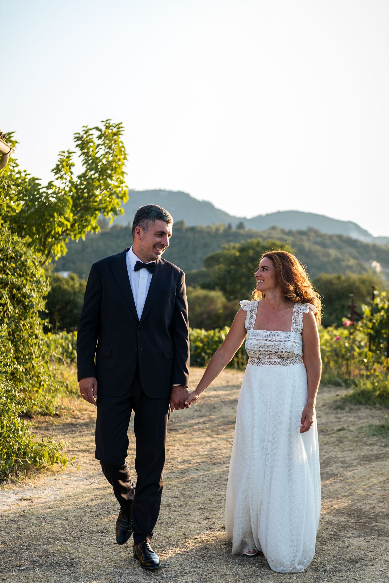 Newlyweds sharing joyful moments while walking along a hilltop vineyard path.