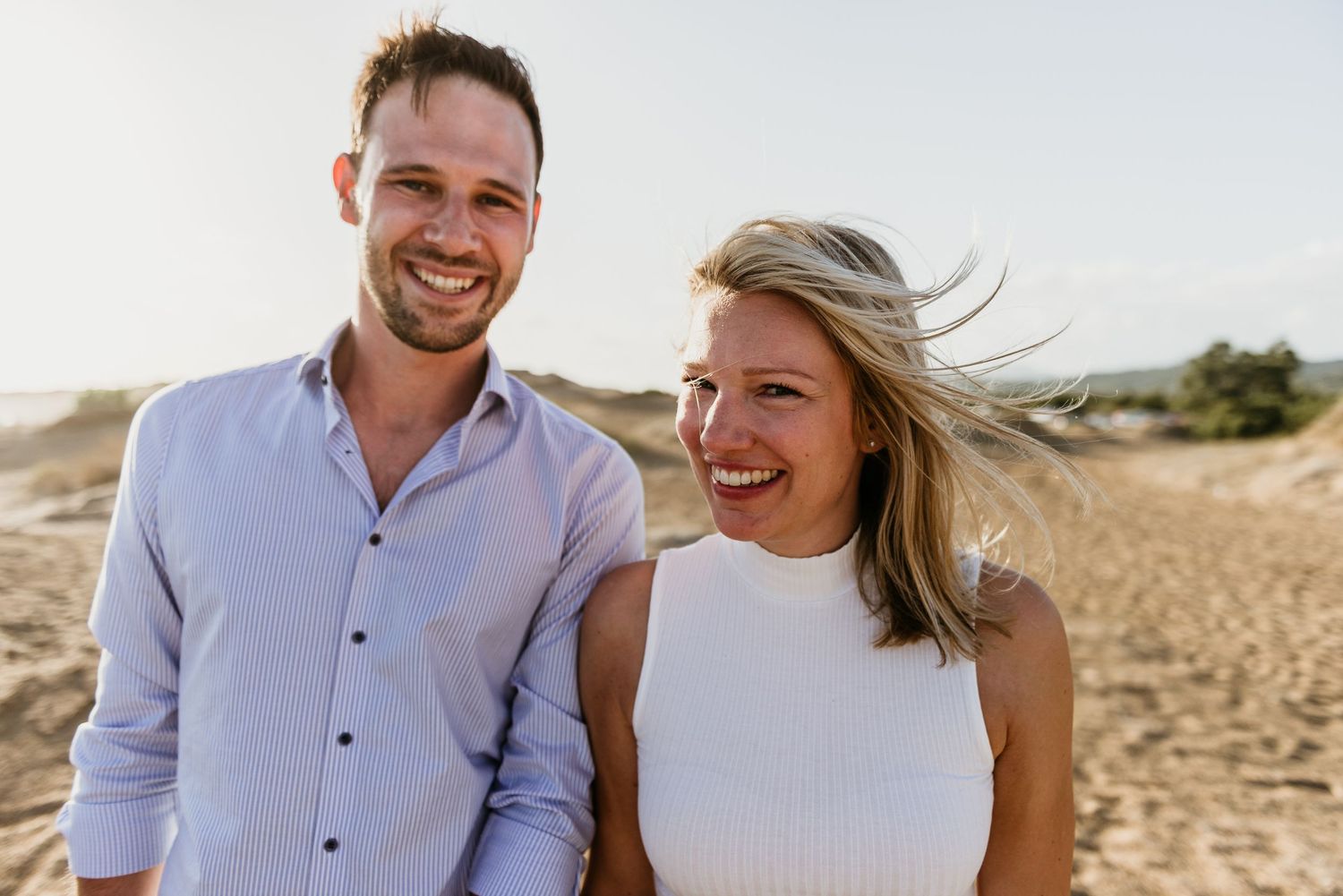 Couple sharing joyful moments on a sunny beach in coordinated white and blue outfits.