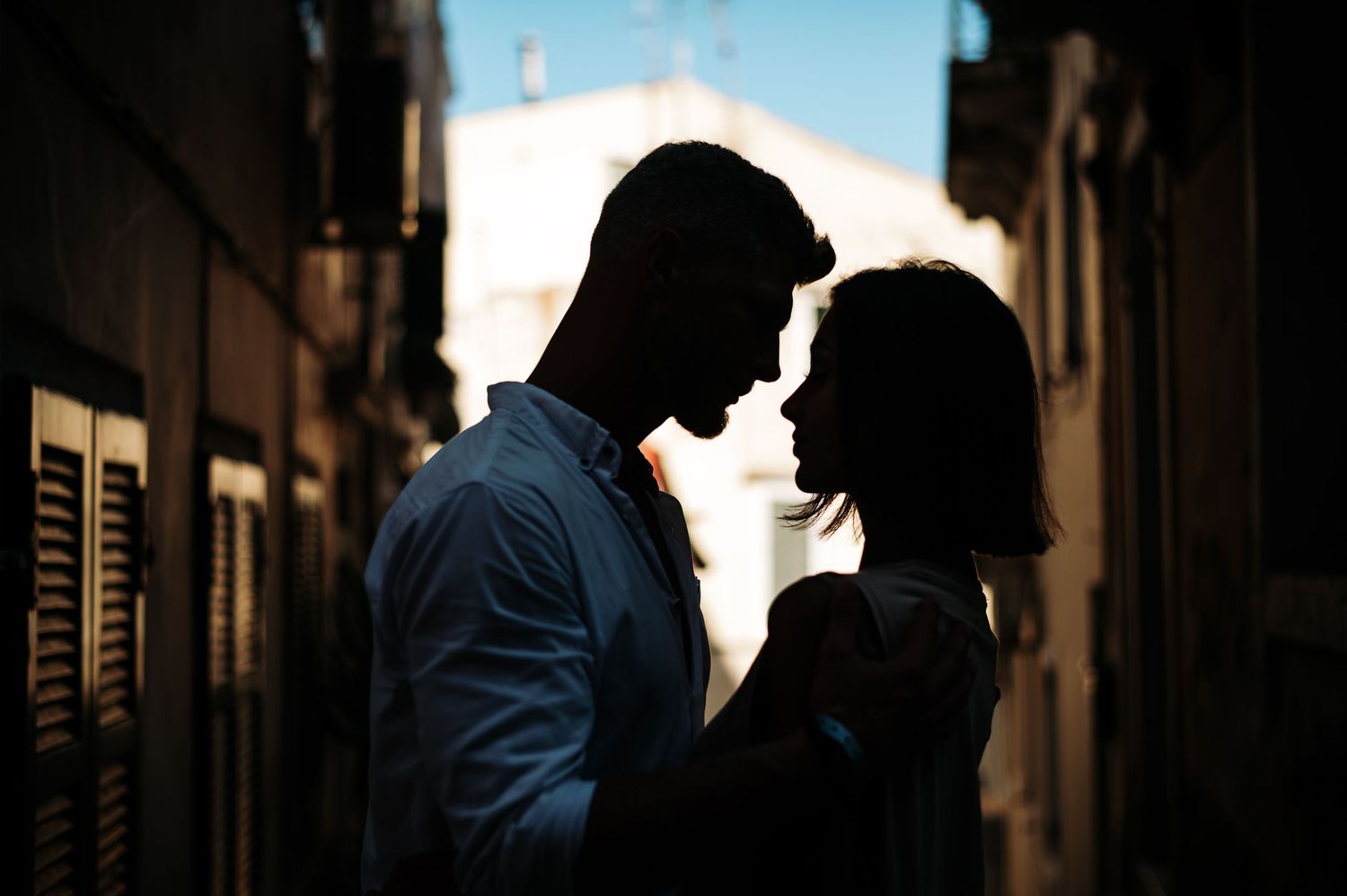 Silhouetted figures in romantic pose against bright backlit urban setting.