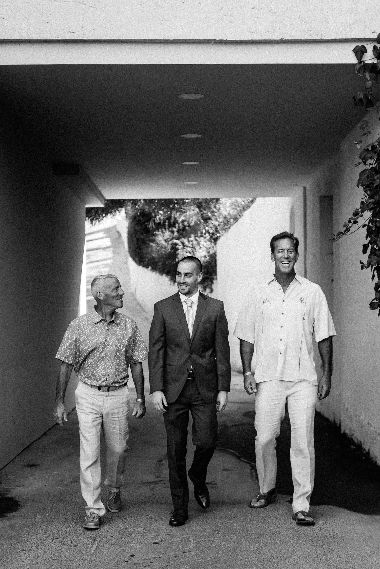 Three men walking together through a white corridor in black and white photography.