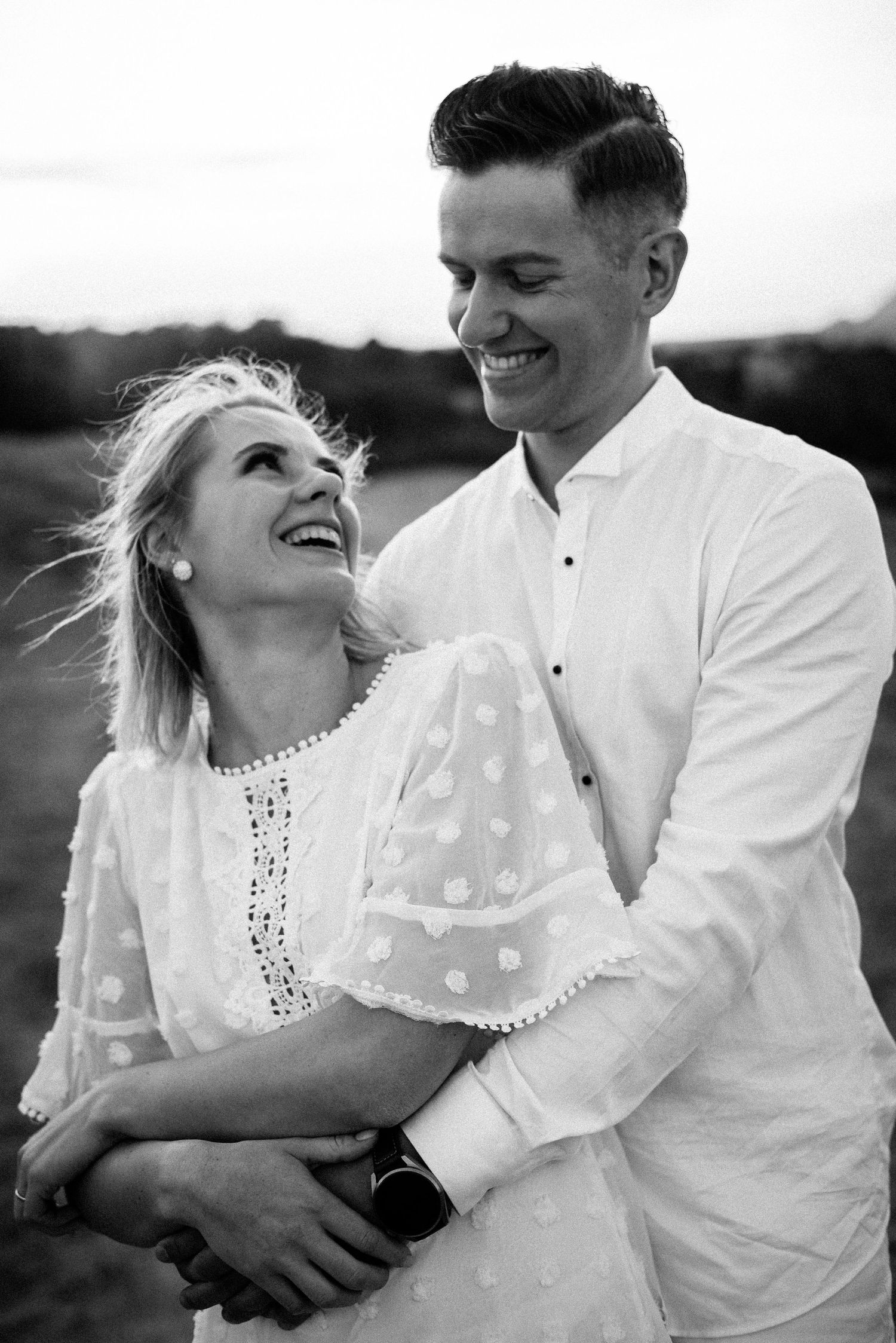 Black and white portrait of a couple laughing together in casual white attire.