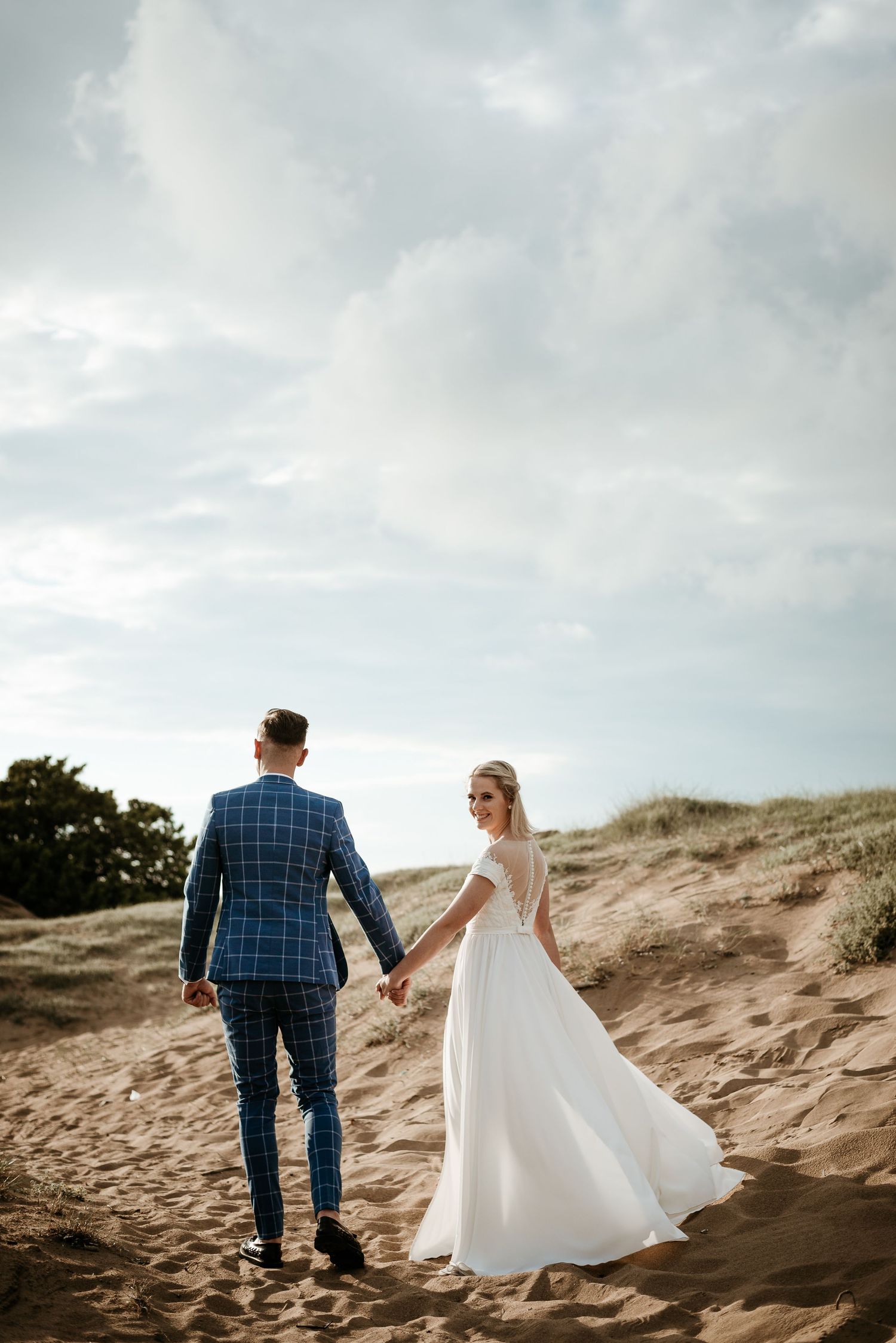Couple walking hand in hand across scenic sand dunes under cloudy skies.