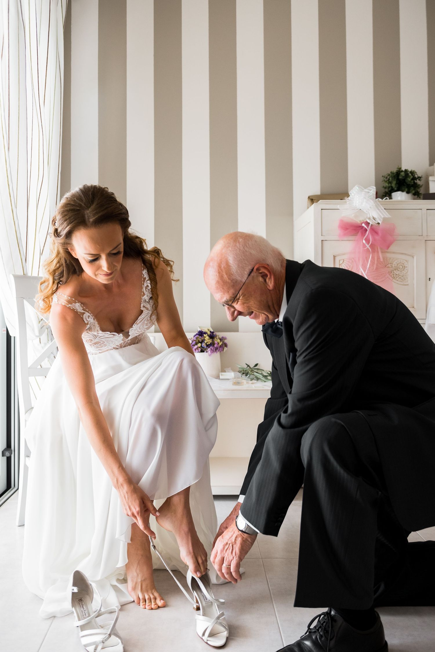 Wedding preparation scene with striped wallpaper showing final dress adjustments.
