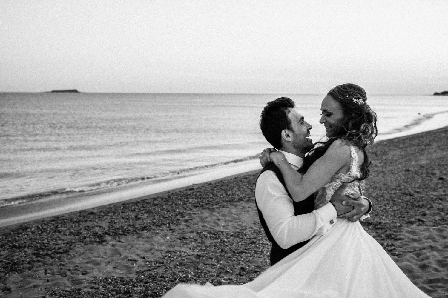 Wedding couple poses for romantic black and white photos along a rocky beach shoreline.