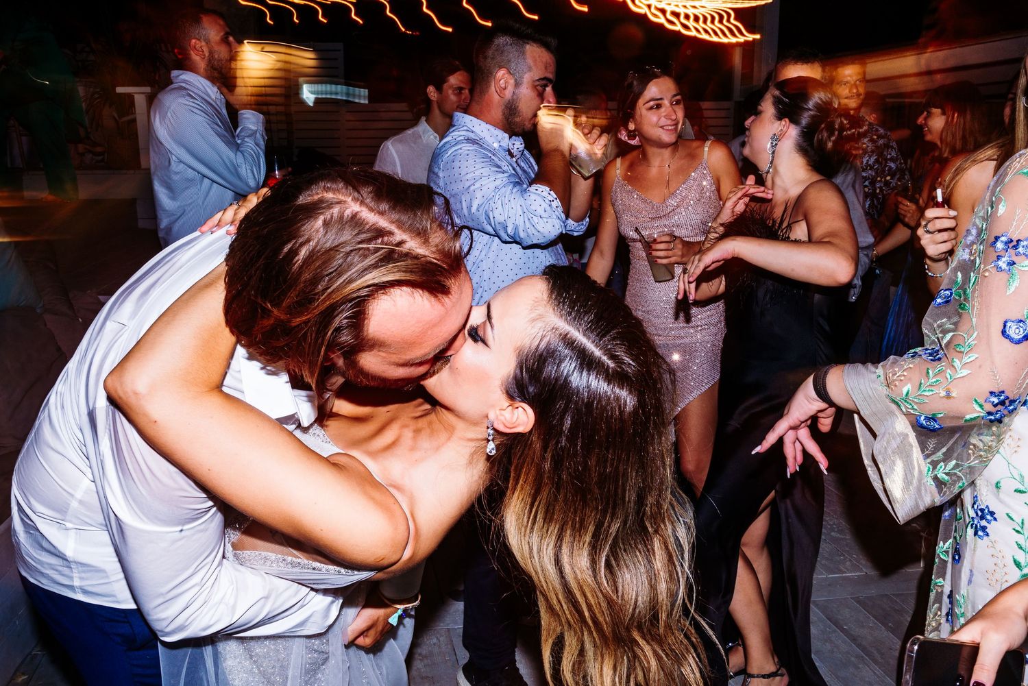 Wedding reception dance floor filled with guests celebrating under ambient lighting.