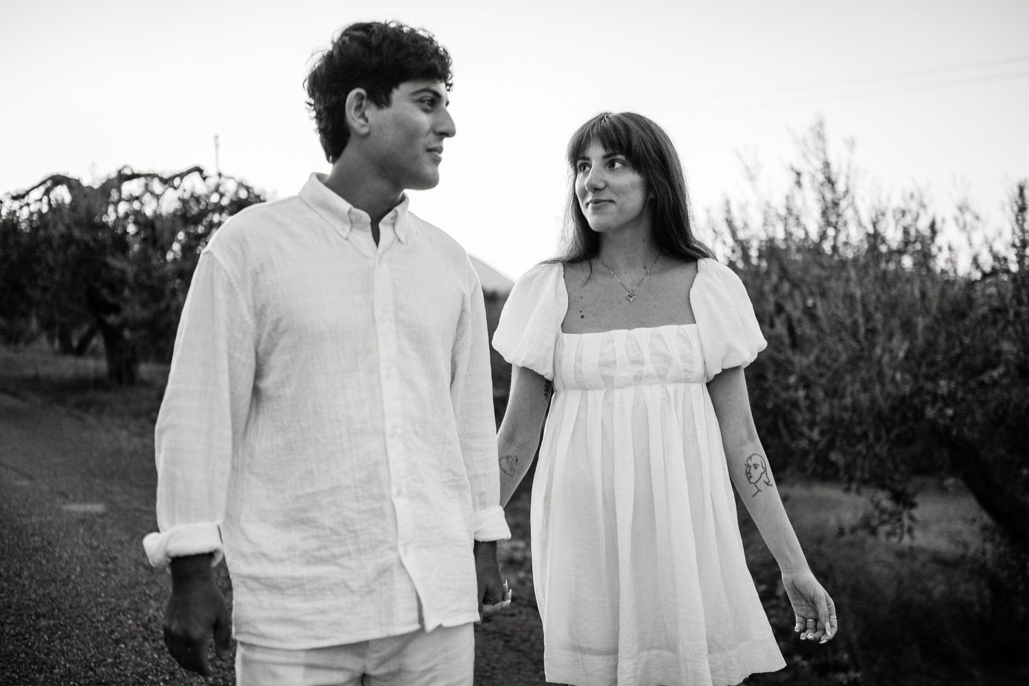 A candid black and white photo of a couple in matching white outfits sharing a joyful moment outdoors.
