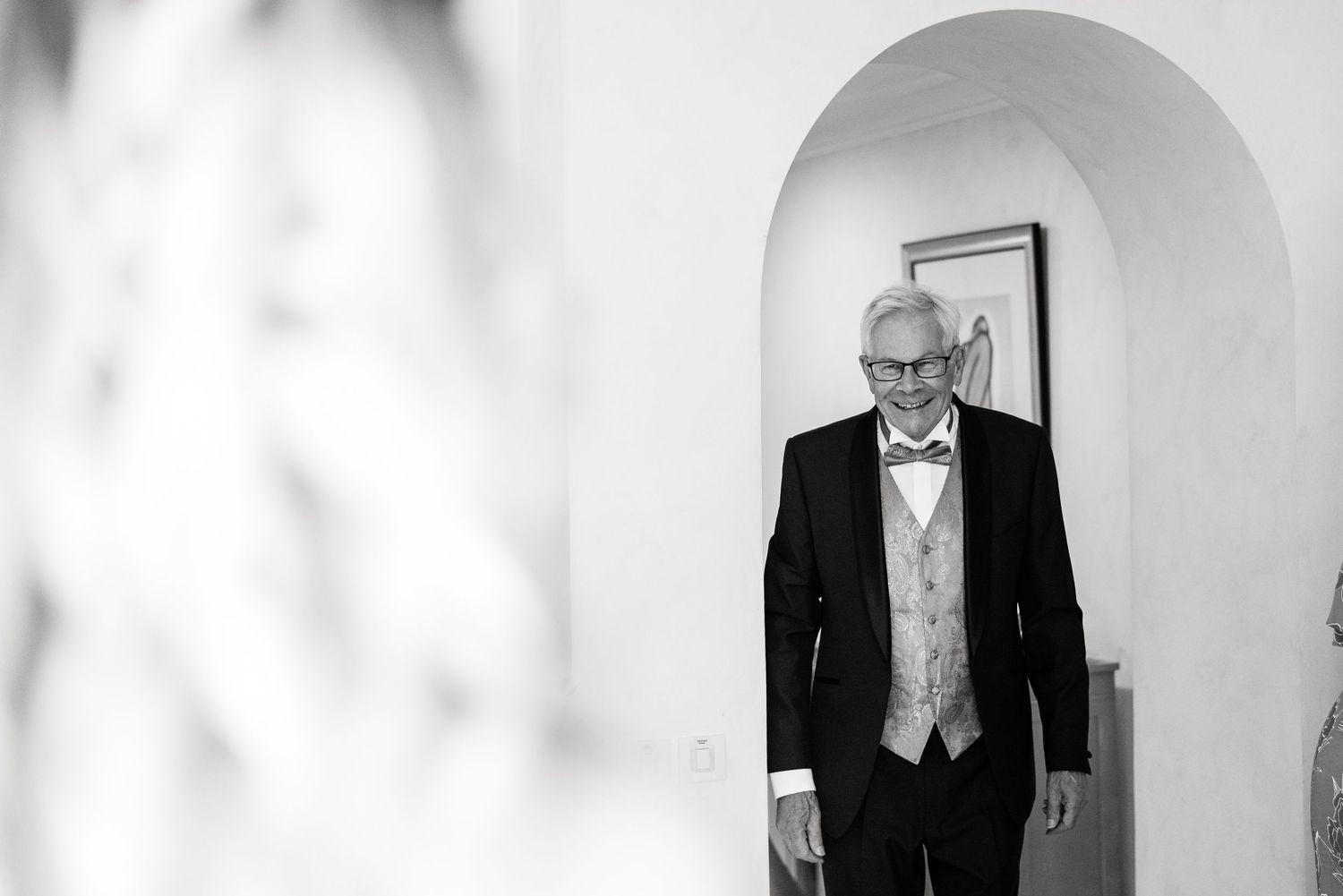 Black and white portrait through arched doorway showing elegant wedding attire.
