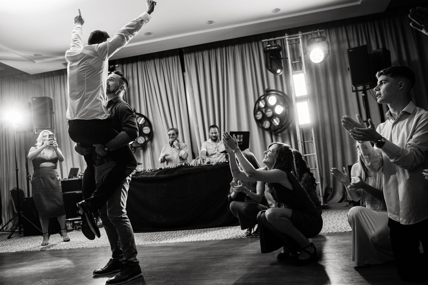 Wedding guests dance in silhouette against white curtains in an elegant venue.
