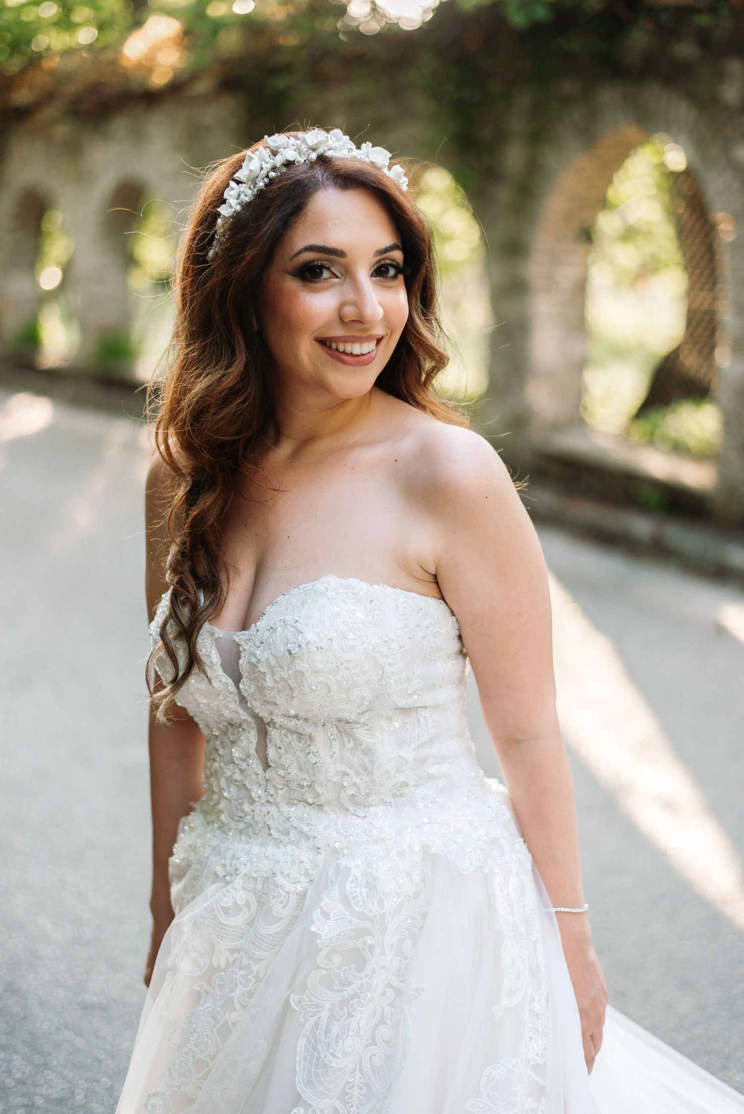 Bride in strapless lace wedding gown poses in golden sunlight.