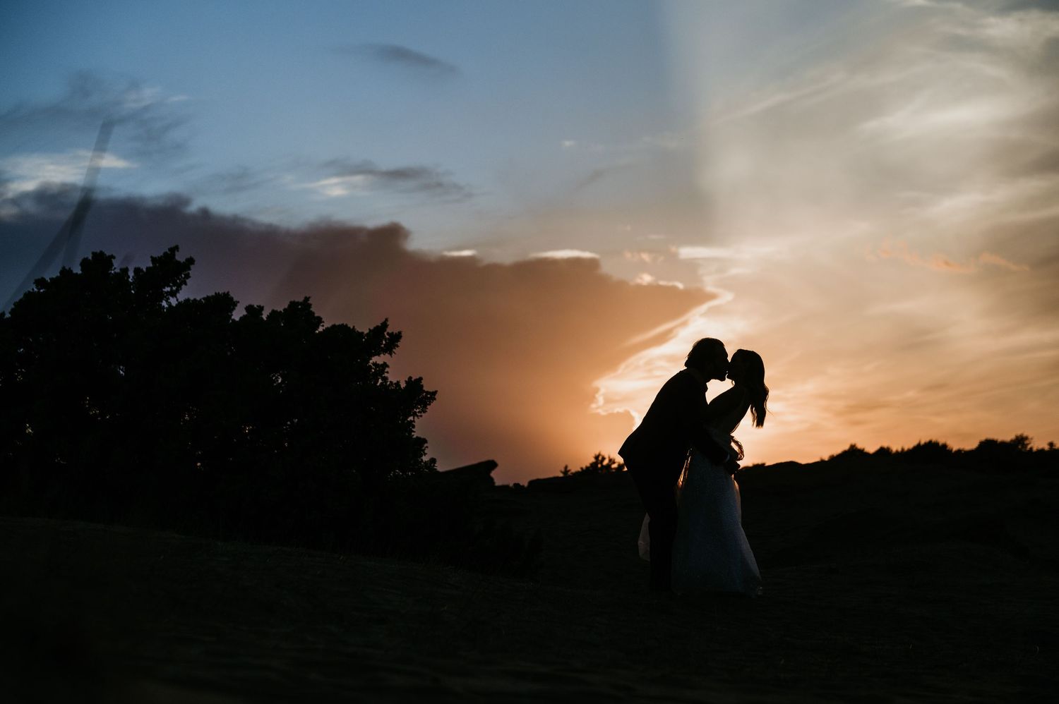 Silhouetted couple embraces against vibrant orange sunset sky.