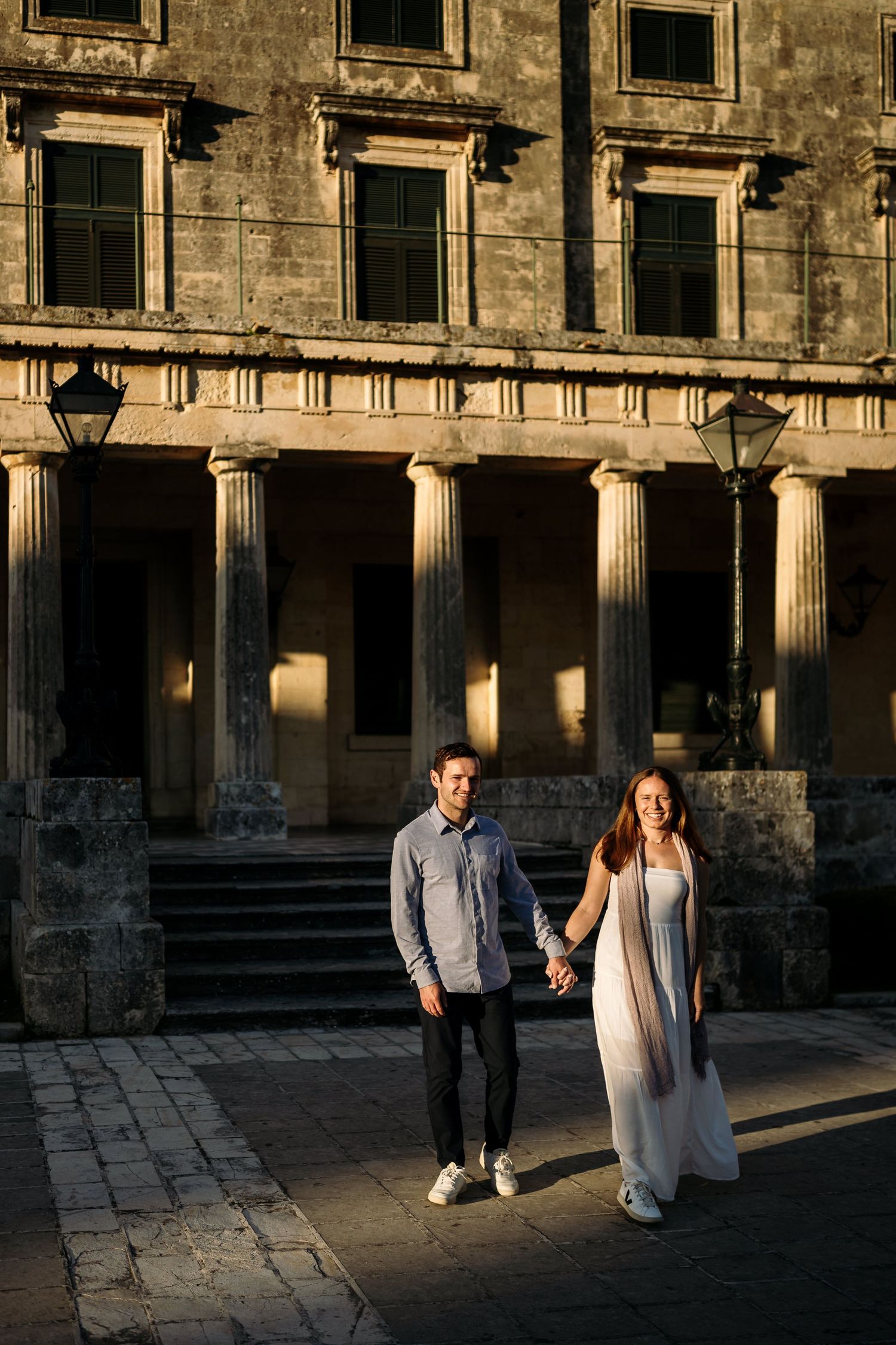 Couple walking through historic stone building with dramatic sunlight and shadows.