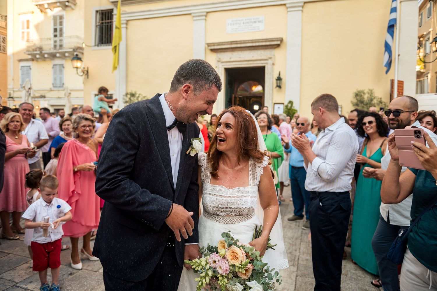 Wedding celebration outside a traditional church with guests throwing confetti.